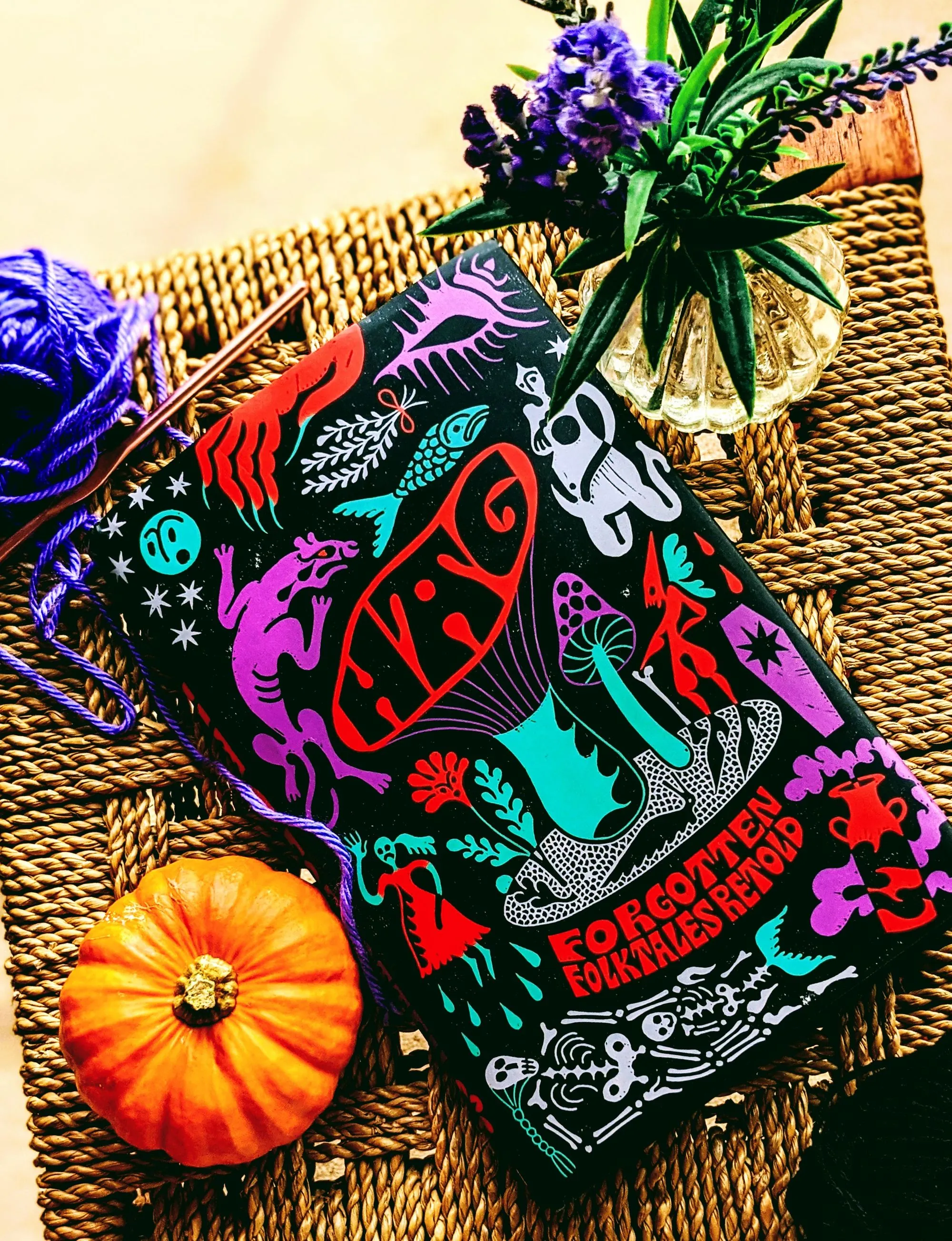 A short-story anthology beside flowers, yarn and a small pumpkin